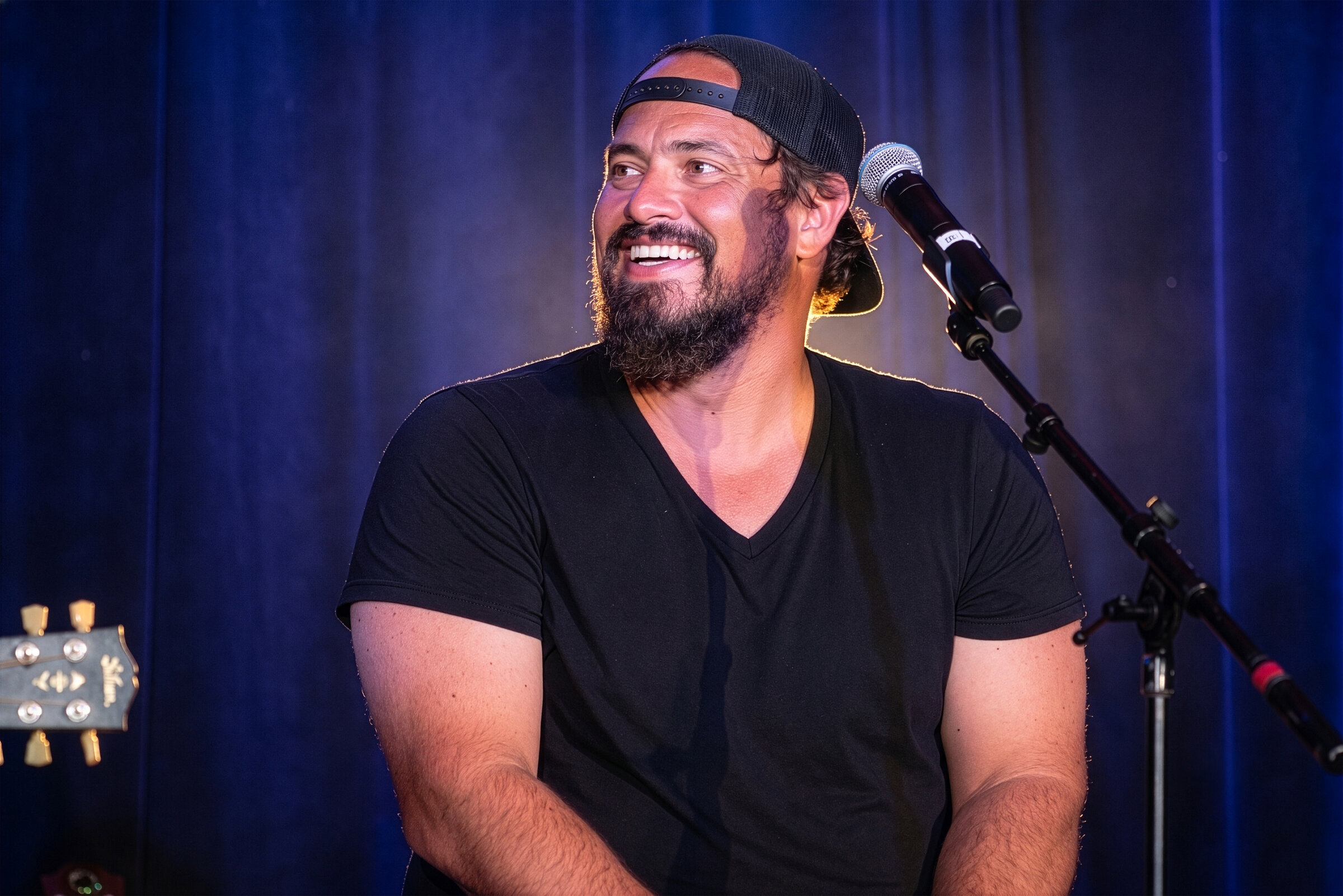 Performer smiling on stage with a microphone and guitar